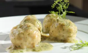 Quattro polpette in bianco su un piatto bianco, condite con una salsa cremosa e erbe aromatiche.