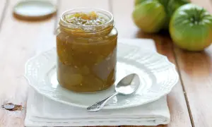 Un vasetto di marmellata di pomodori verdi, con pomodori verdi sullo sfondo.