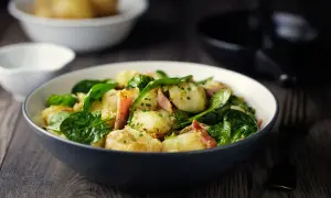 Insalata di patate con spinacini freschi e pancetta croccante, condita con erbe aromatiche. Un piatto gustoso e colorato.