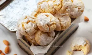 Biscotti con farina di mandorle, spolverati di zucchero a velo, in una scatola vintage. Alcune mandorle intere sono sparse intorno.