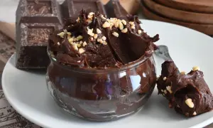 Un delizioso budino al cioccolato, cremoso e guarnito con nocciole tritate, accanto a una tavoletta di cioccolato fondente.