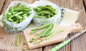 Fagiolini freschi in sacchetti trasparenti, pronti per essere preparati. Un tagliere di legno e un coltello suggeriscono come congelare i fagiolini per conservarli.