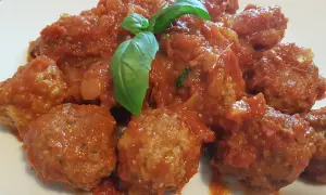 Un piatto invitante di polpette di carne morbide immerse in un sugo rosso ricco, guarnite con una foglia di basilico fresco.