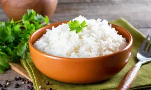 Un invitante piatto di riso in bianco, guarnito con prezzemolo fresco, su un tovagliolo verde. Accanto, grani di pepe e una forchetta.