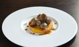 Delizioso riso al salto con bocconcini di carne e salsa bruna, guarnito con erbe fresche su un piatto bianco.