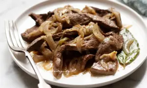Piatto di fegato alla veneziana con cipolle caramellate, servito su un piatto bianco con una forchetta.