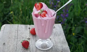 Un bicchiere di cremoso gelato alla fragola, guarnito con fragole fresche, su un tavolo di legno rustico.
