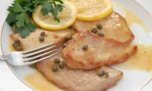 Scaloppine al limone succulente, guarnite con capperi, prezzemolo fresco e fette di limone. Una forchetta attende il primo assaggio.