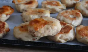 Polpette di pollo dorate e gustose, appena sfornate, con formaggio fuso e pezzetti di carne visibili.