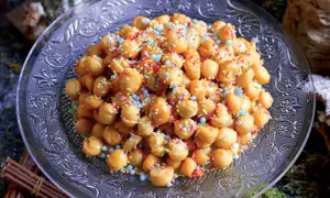 Struffoli ricetta della nonna: palline dorate fritte, ricoperte di miele e confettini colorati, su un piatto decorato.