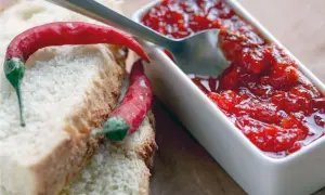 Fette di pane con peperoncini rossi e una ciotolina di marmellata di peperoncino, pronta per essere gustata.