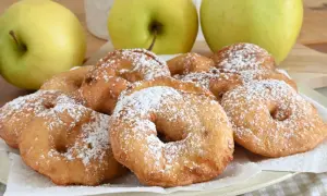 Frittelle di mele dorate e zuccherate, pronte per essere gustate. Tre mele verdi sullo sfondo.