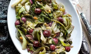 Scarola in padella con olive nere e pinoli, un contorno saporito e colorato, pronto per essere gustato.
