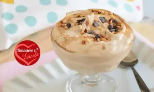 Deliziosa mousse al caffè, guarnita con nocciole tostate e gocce di cioccolato, servita in una coppa di vetro.