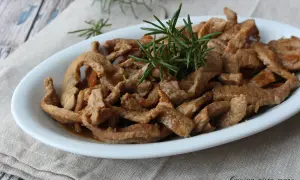 Deliziosi straccetti di vitello saltati, guarniti con rosmarino fresco, serviti in un piatto bianco su un tovagliolo di lino.