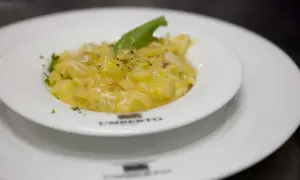 Un piatto di pasta e patate cremoso, guarnito con basilico fresco e pepe nero, servito in un elegante piatto bianco.