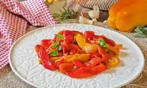 Peperoni rossi e gialli arrostiti in friggitrice ad aria, guarniti con basilico fresco, su un piatto bianco decorato.