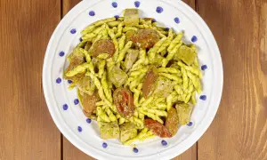 Piatto di trofie alla carlofortina con tonno, pomodorini secchi e pesto, servito su un piatto bianco con decorazioni blu.