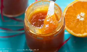 Un vasetto di marmellata di arance fatto in casa, con una fetta d'arancia accanto. La marmellata è lucida e invitante, pronta per essere gustata.