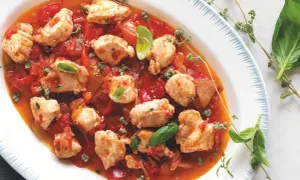 Piatto di coniglio alla cacciatora con pezzi di carne tenera in salsa di pomodoro e peperoni, guarnito con basilico fresco e erbe aromatiche.