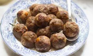 Polpette dorate e succulente in friggitrice ad aria, servite su un piatto di ceramica blu e bianco.