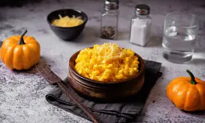 Un invitante piatto di pasta e zucca, guarnito con formaggio grattugiato, accanto a piccole zucche arancioni.