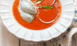 Una cremosa zuppa di pomodoro, arricchita da due quenelle di burrata e foglie di basilico fresco. Un piatto invitante e gustoso.