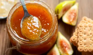 Un cucchiaio raccoglie la deliziosa marmellata di fichi da un barattolo, accanto a fichi freschi e biscotti.