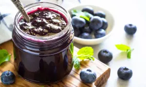 Vasetto di marmellata di mirtilli fatto in casa, con mirtilli freschi e foglie di menta su un tagliere di legno.