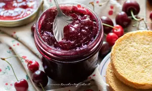 Un barattolo pieno di marmellata di ciliegie fatta in casa, con ciliegie fresche e fette biscottate.
