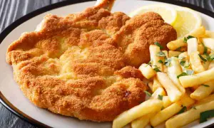 Cotoletta alla milanese dorata e croccante, servita con patatine fritte e spicchi di limone.