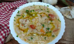 Un piatto fumante di riso e fagioli, condito con olio d'oliva e prezzemolo, con aglio e una tovaglia a scacchi sullo sfondo.