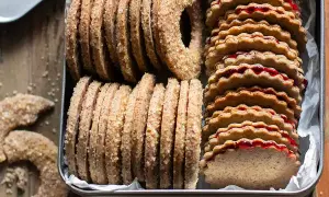 Biscotti grano saraceno ripieni di marmellata, impilati in una scatola di latta. Alcuni biscotti a forma di ciambella e a mezzaluna sono sparsi sul tavolo.
