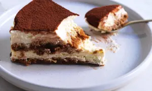Una fetta di tiramisù ricetta originale, con strati di savoiardi, crema al mascarpone e cacao in polvere. Un cucchiaino ne ha già assaggiato un pezzetto.
