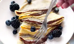 Piatto di crepes alla Nutella, guarnite con mirtilli e more, pronte per essere gustate.