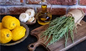 Asparagi di mare freschi, limoni, aglio e olio d'oliva su un tagliere di legno, pronti per una ricetta saporita.