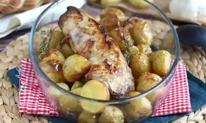 Un succulento filetto di maiale al forno, dorato e profumato, circondato da patate novelle arrosto e rametti di rosmarino in una ciotola di vetro.