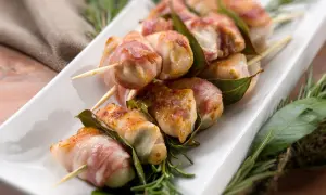 Involtini di lonza avvolti in pancetta, infilzati su spiedini con foglie di alloro e rosmarino.