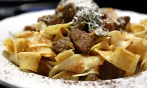 Pappardelle al cinghiale fumanti, con pezzi di carne succulenta e una spolverata di parmigiano.