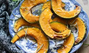 Fette di zucca in friggitrice ad aria, dorate e profumate al rosmarino, servite su un piatto blu e bianco.