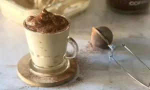 Deliziosa crema al caffè, spolverata di cacao, servita in una tazza di vetro con un colino per caffè accanto.