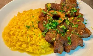 Un piatto di ossobuco alla milanese con risotto giallo, guarnito con prezzemolo fresco e scorza di limone.