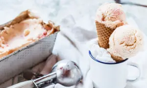 Due palline di gelato fatto in casa, con pezzetti di frutta, in un cono, accanto a una vaschetta e un porzionatore.