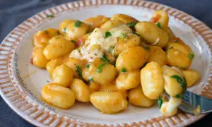 Gnocchi di spinaci cremosi con formaggio filante e prezzemolo fresco, serviti su un piatto decorato.