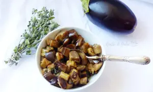 Melanzane in padella, un contorno saporito, con un mazzetto di erbe aromatiche e una melanzana intera.