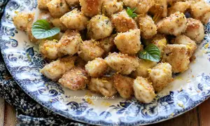 Bocconcini di pollo dorati e croccanti, guarniti con scorza di limone e foglioline di menta, su un piatto decorato.