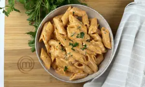 Penne alla vodka cremose e invitanti, guarnite con prezzemolo fresco, su un tagliere di legno con il logo di MasterChef.