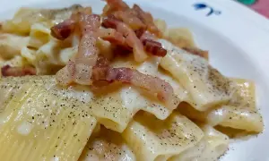 Un piatto di pasta alla gricia fumante, con guanciale croccante e abbondante pepe nero.