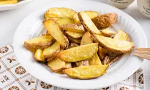Patate a spicchi dorate e croccanti, appena sfornate dalla friggitrice ad aria, servite su un piatto bianco.
