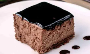 Un delizioso semifreddo al cioccolato, con una lucida glassa scura e gocce di salsa al cioccolato sul piatto bianco.